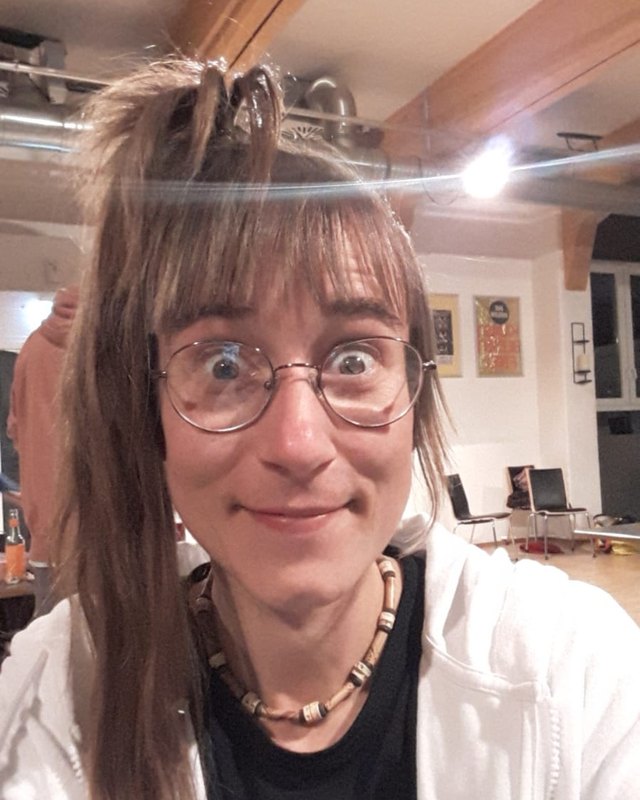 Tina Galinsky mit Brille und großen Augen, verschmitzt lächelnd